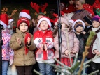 przedszkolaki w mikołajkowych czapkach stoją na scenie, śpiewają kolędy 