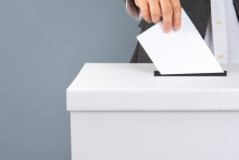 grafika poglądowa dłoń wrzuca kartkę do urny wyborczej