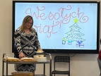 pracownica ŚDS Michalina stoi przy wózku gastronomicznym i kroi ciasto w tle monitor z ozdobnym napisem Wesołych Świąt